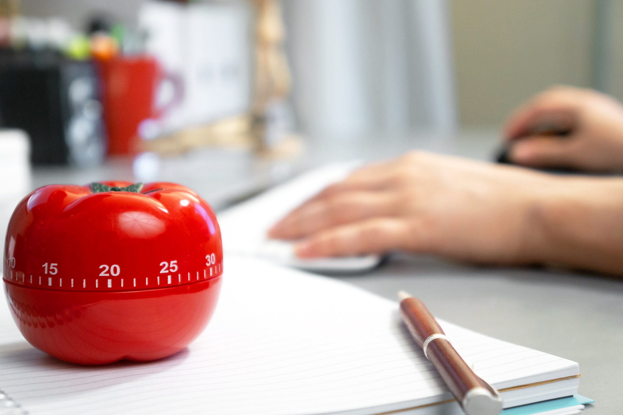 Tomato-shaped timer on notebook and pen, representing Pomodoro Technique for kids’ math focus.